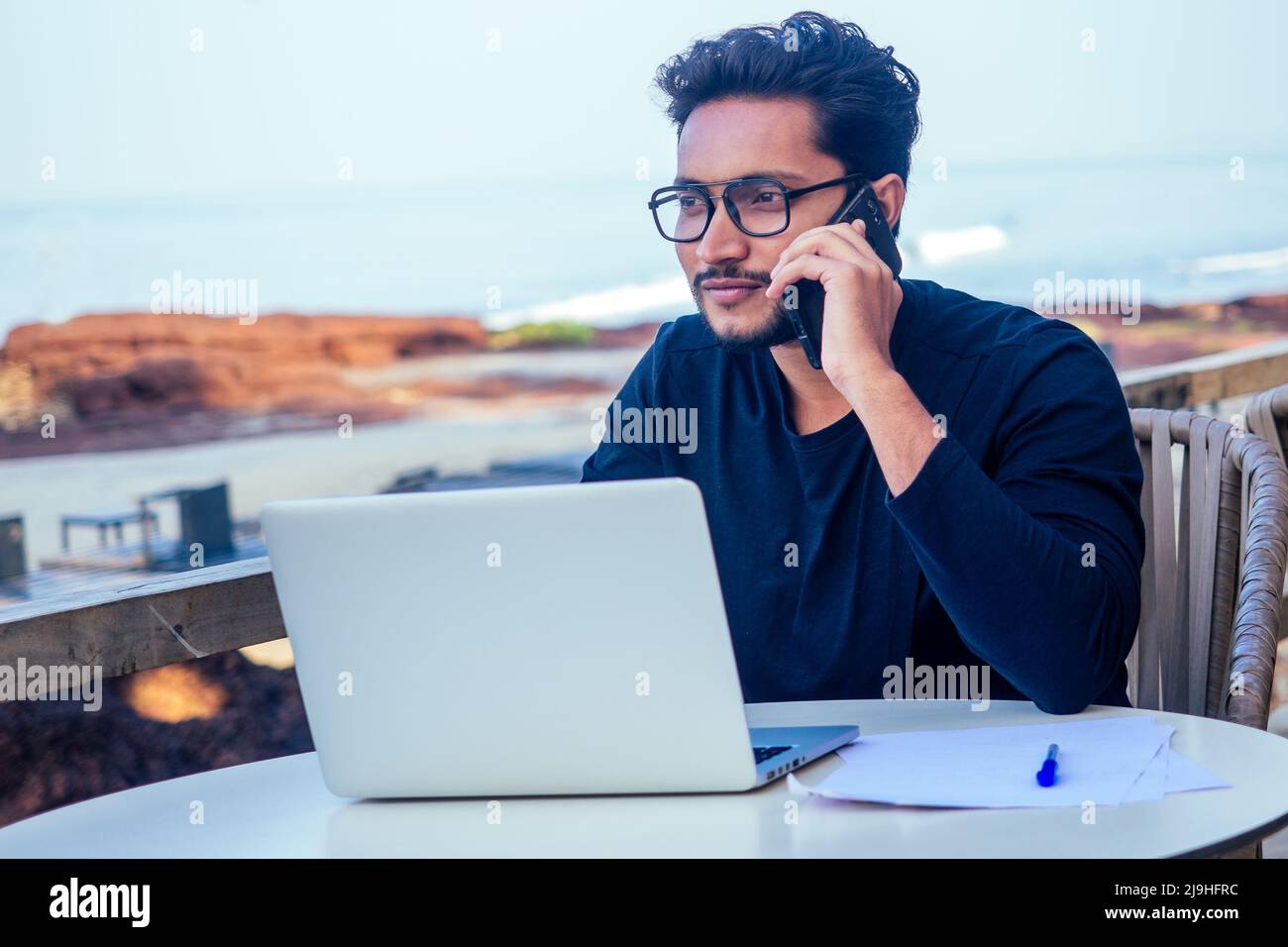Mann, der am Telefon spricht indien Sommerferien.stilvolle junge indische männliche Freiberufler arbeitet mit Laptop freiberuflich Surfen online.Geschäftsmann an Remote Stockfoto