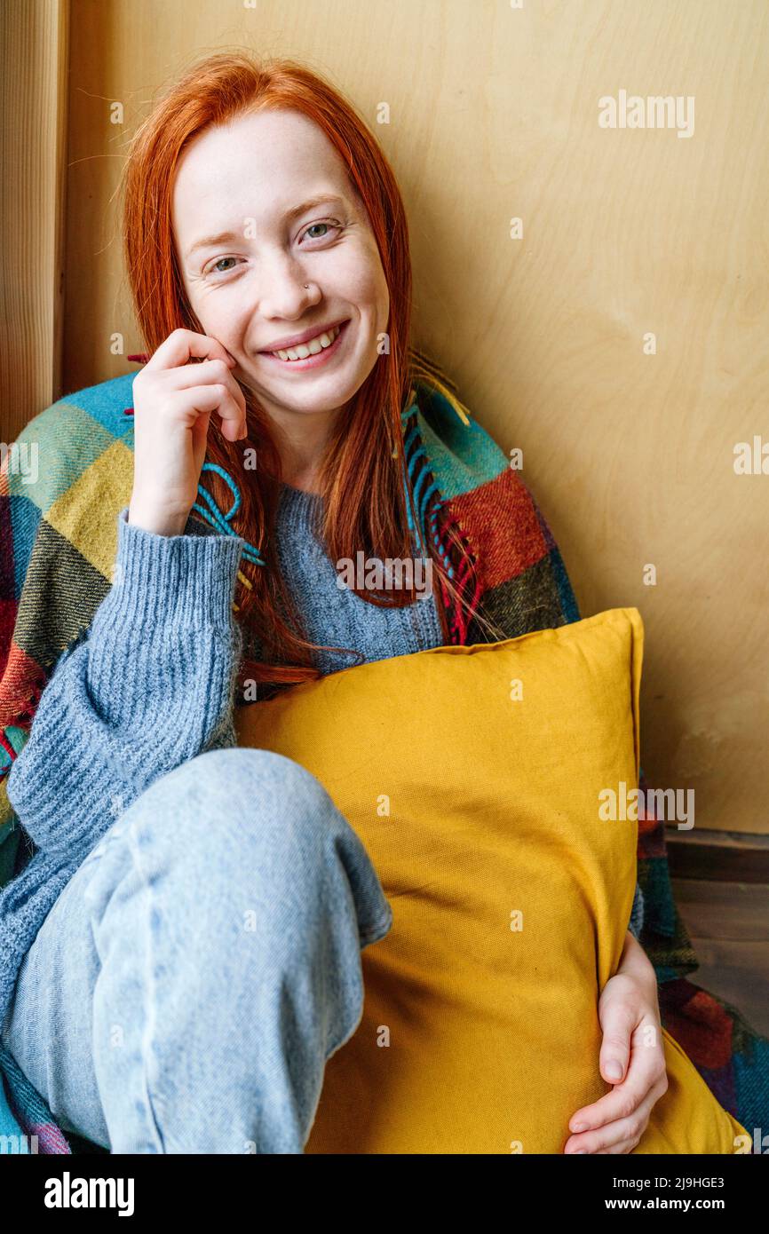 Lächelnde junge Frau mit Kissen vor der Wand Stockfoto