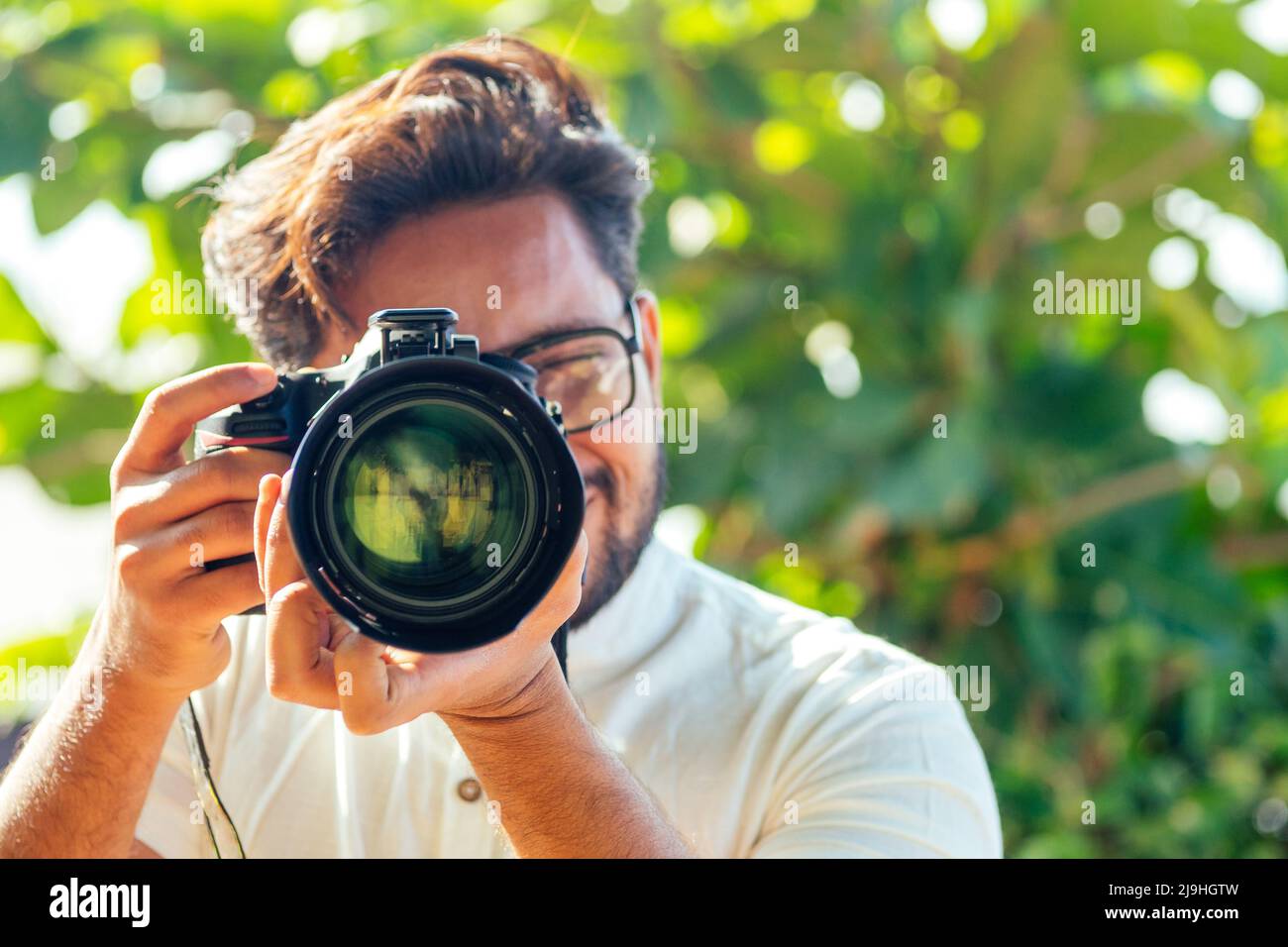 Ein hübscher und selbstbewusster indischer Fotograf mit einer großen professionellen Kamera, die am Strand fotografiert.Fotosession im Sommer Stockfoto