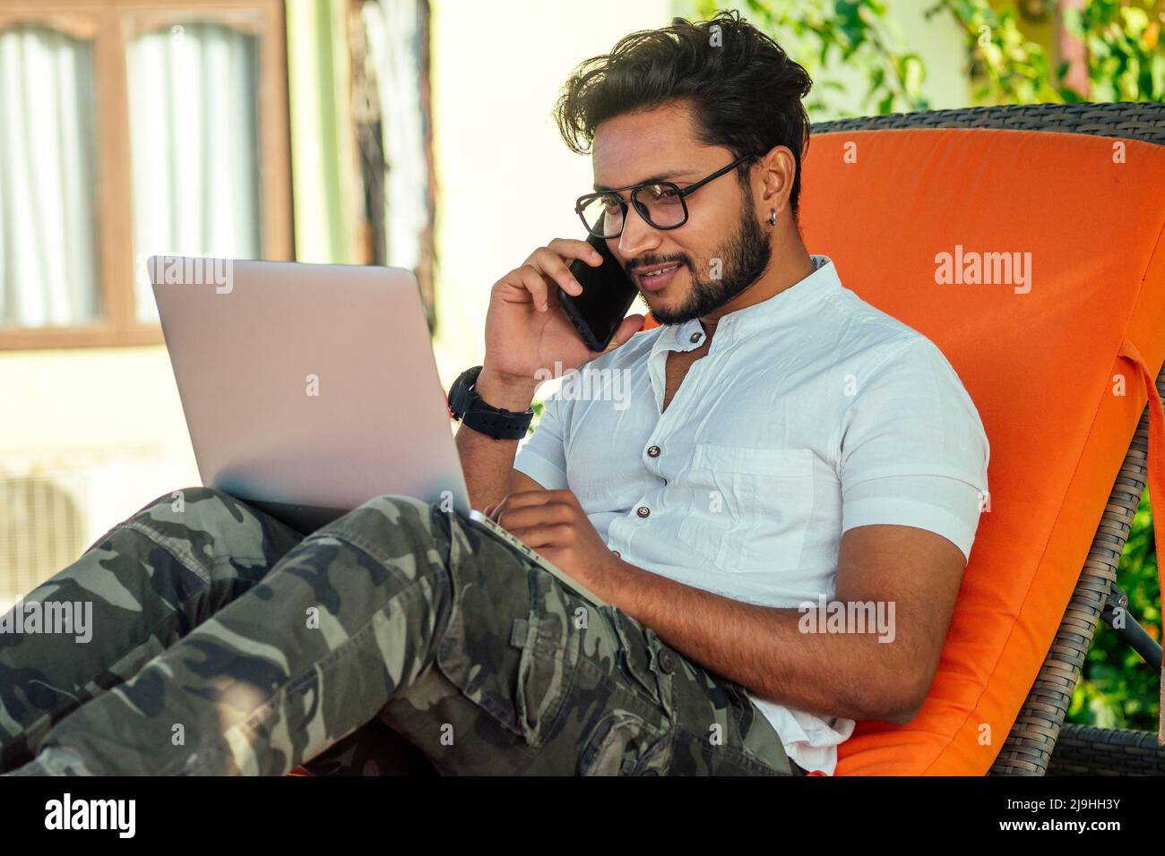 Mann, der am Telefon spricht indien Sommerferien.stilvolle junge indische männliche Freiberufler arbeitet mit Laptop freiberuflich Surfen online.Geschäftsmann an Remote Stockfoto