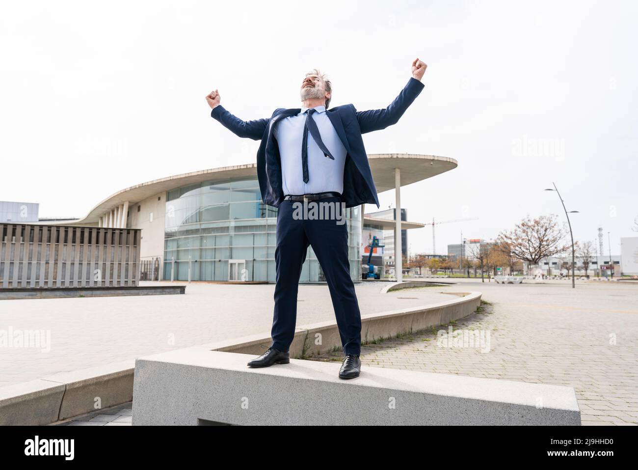 Fröhlicher Geschäftsmann, der an der Wand im Büropark steht Stockfoto