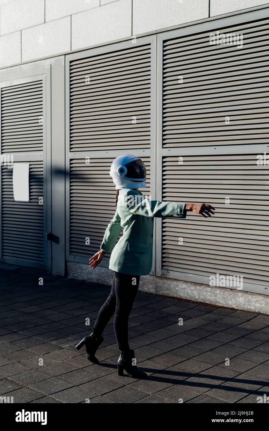 Junge Geschäftsfrau trägt Weltraumhelm tanzen auf dem Fußweg Stockfoto