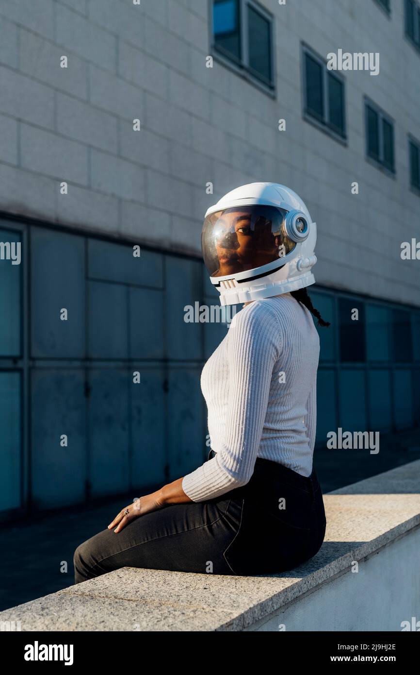 Junge Geschäftsfrau mit Weltraumhelm an der Wand sitzen Stockfoto