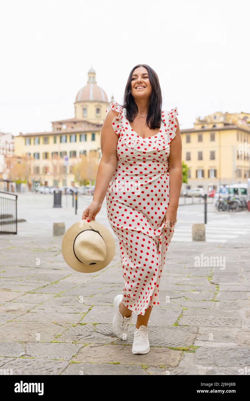 Lächelnde kurvige Frau in einem gepunkteten Kleid in der Stadt Stockfoto