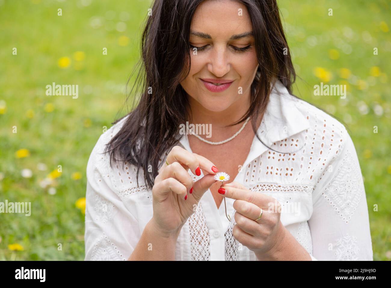 Lächelnde Frau mit langen schwarzen Haaren hält Gänseblümchen Blume Stockfoto