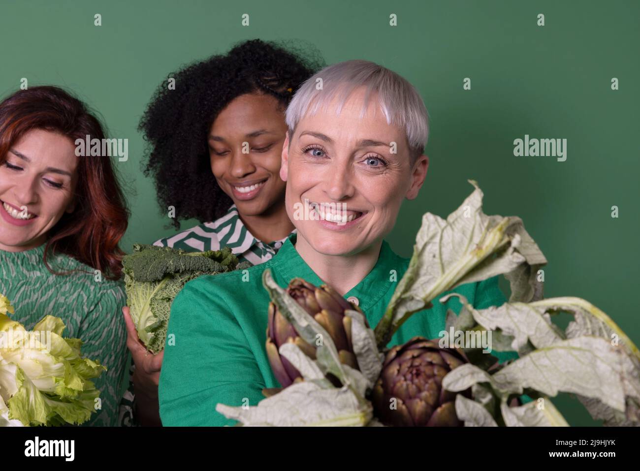 Glückliche multirassische Freunde mit frischem rohem Gemüse vor grünem Hintergrund Stockfoto