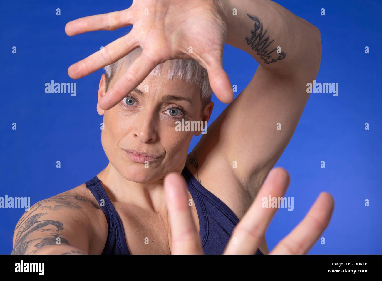 Frau mit kurzen Haaren gestikuliert vor blauem Hintergrund Stockfoto