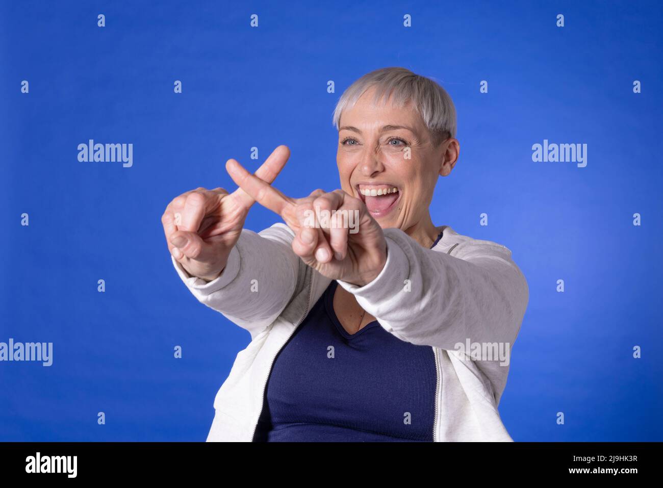 Glückliche Frau, die Kreuzzeichen mit Fingern vor blauem Hintergrund macht Stockfoto