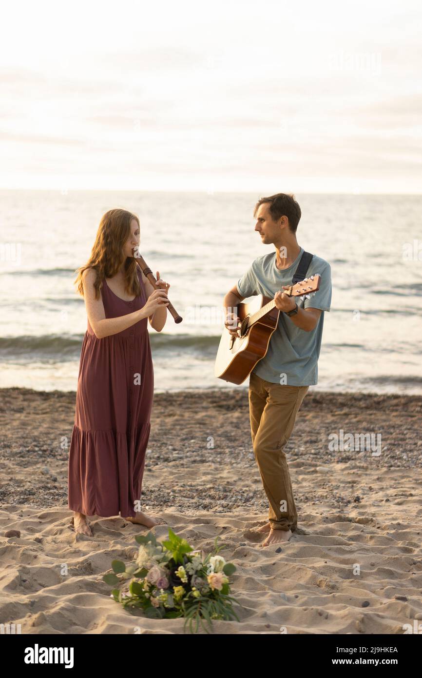 Frau spielt Flöte von Mann mit Gitarre am Strand Stockfoto