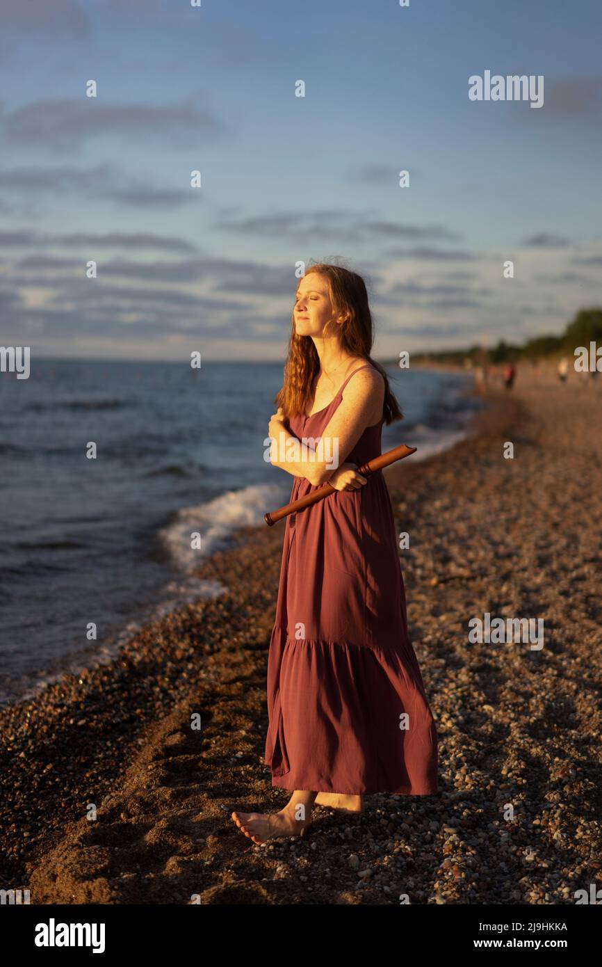 Lächelnde Frau mit gekreuzten Armen, die Flöte am Strand hält Stockfoto