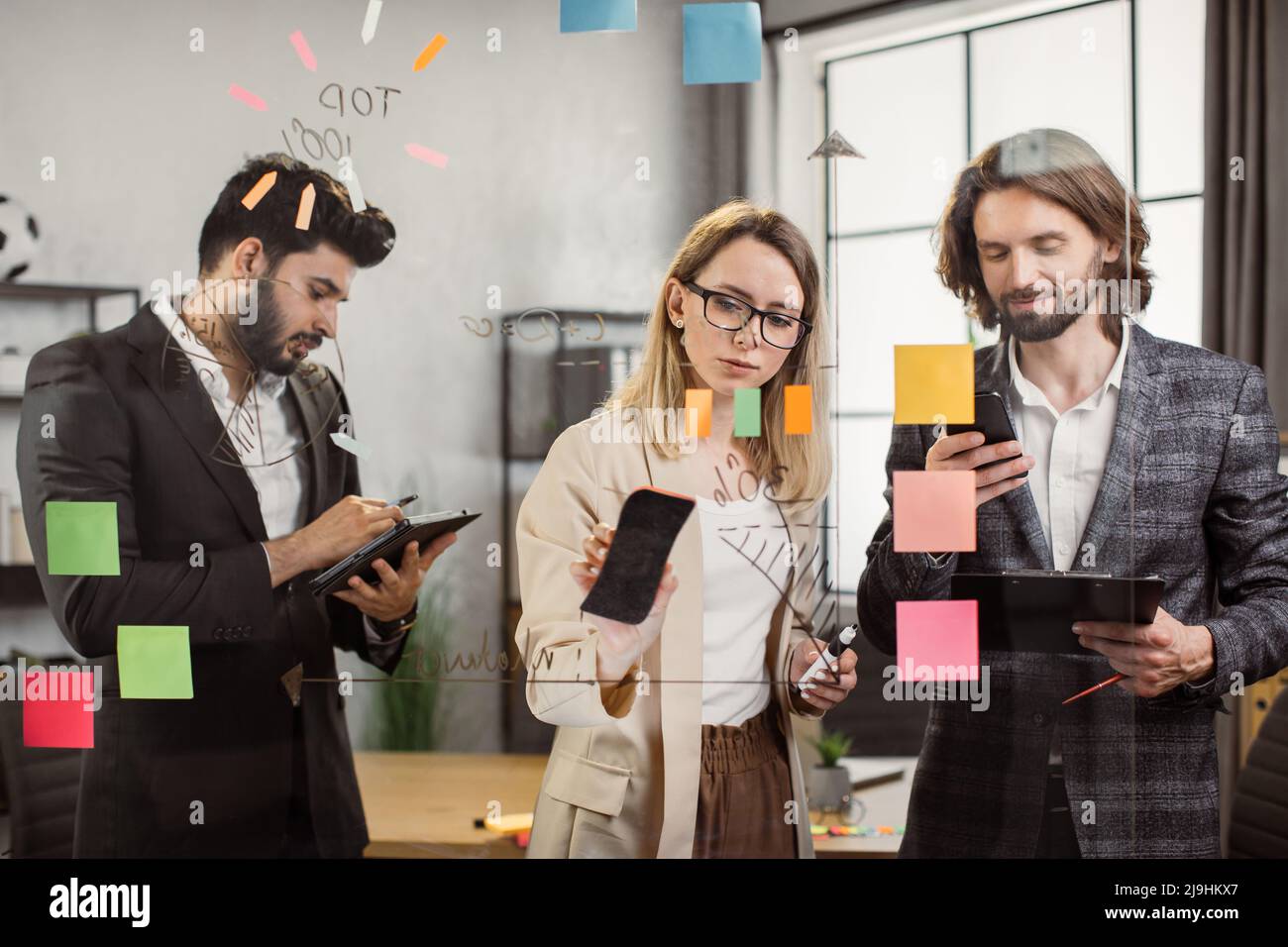 Teamarbeit multiethnischer Manager in formeller Kleidung mit modernem Tablet, Smartphone und Clipboard während eines produktiven Meetings in geräumigen Büros. Konzept von digitalen Geräten, Menschen und Unternehmen. Stockfoto