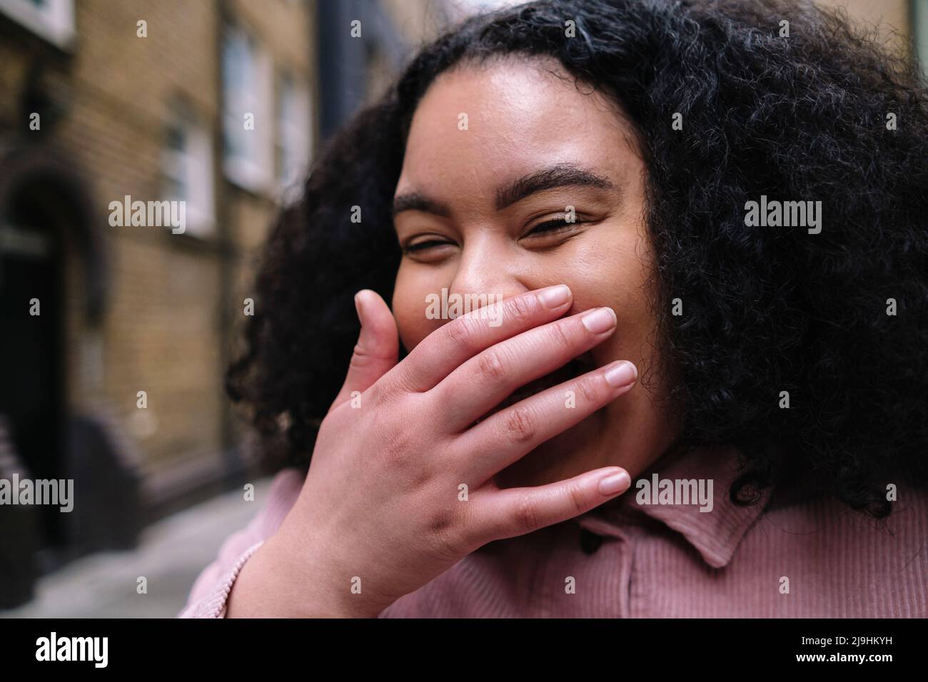 Fröhliche junge Frau, die mit der Hand über dem Mund lachend ist Stockfoto
