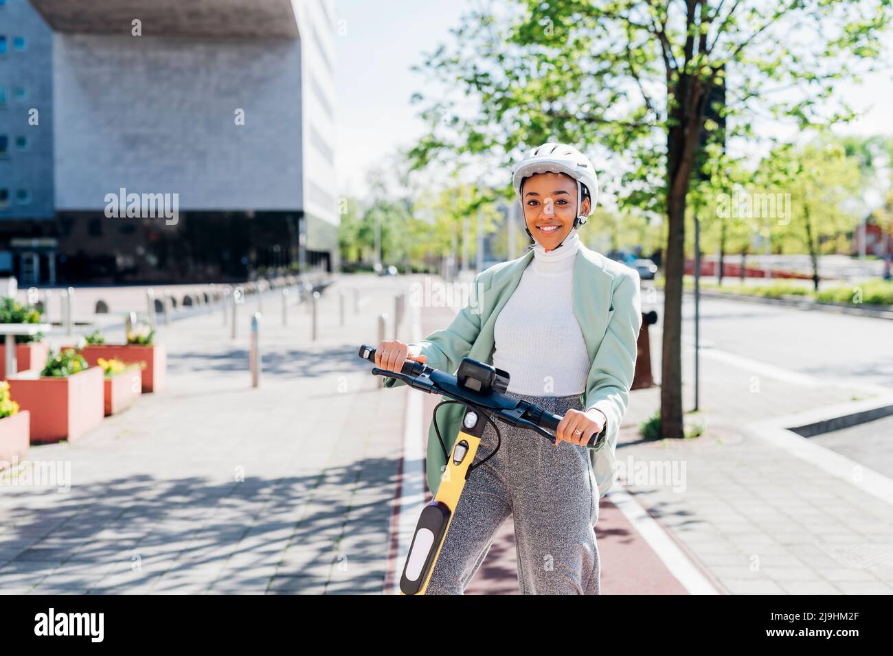 Junge Geschäftsfrau mit Elektro-Roller auf dem Fußweg Stockfoto