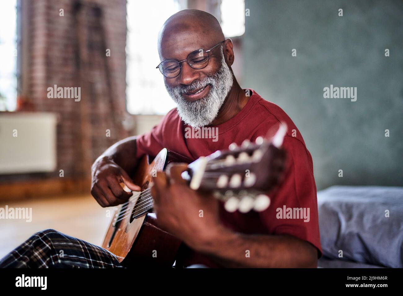 Lächelnder reifer Mann, der zuhause Gitarre spielt Stockfoto