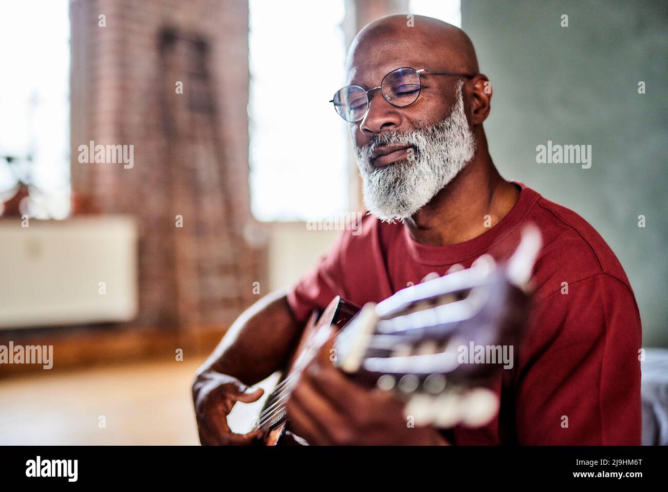 Mann mit geschlossenen Augen spielt Gitarre zu Hause Stockfoto
