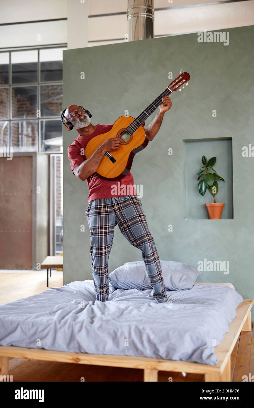 Mann mit Gitarre imitiert Rockmusiker auf dem Bett zu Hause Stockfoto