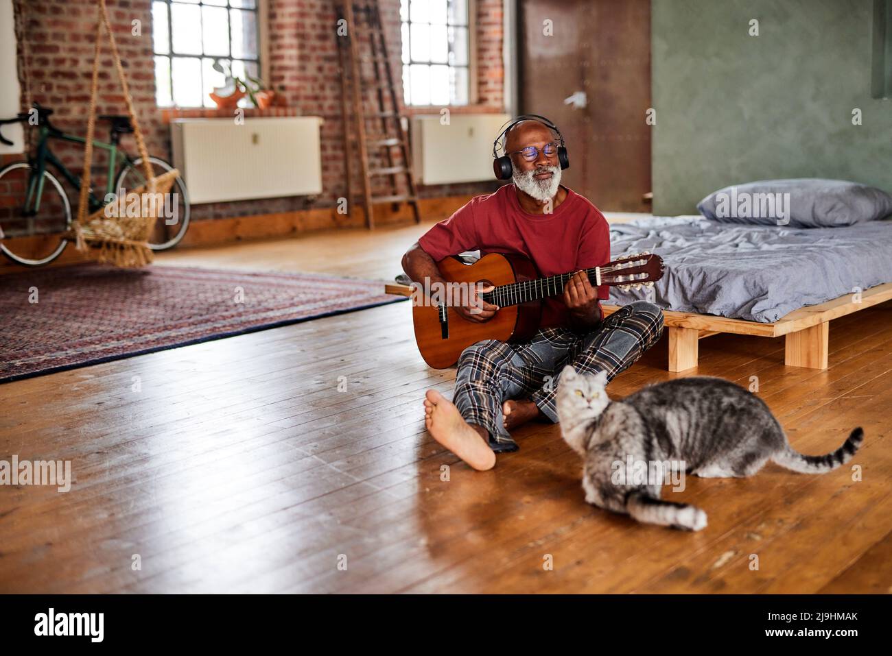 Reifer Mann spielt Gitarre von Katzen im Schlafzimmer zu Hause Stockfoto