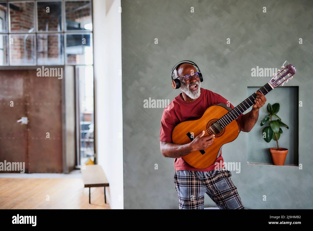Mann mit Kopfhörern, der zu Hause Gitarre spielt und singt Stockfoto