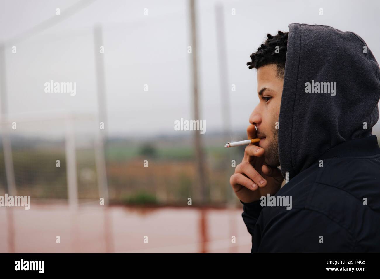 Junger Mann mit Kapuzenhemd, der Zigarette raucht Stockfoto