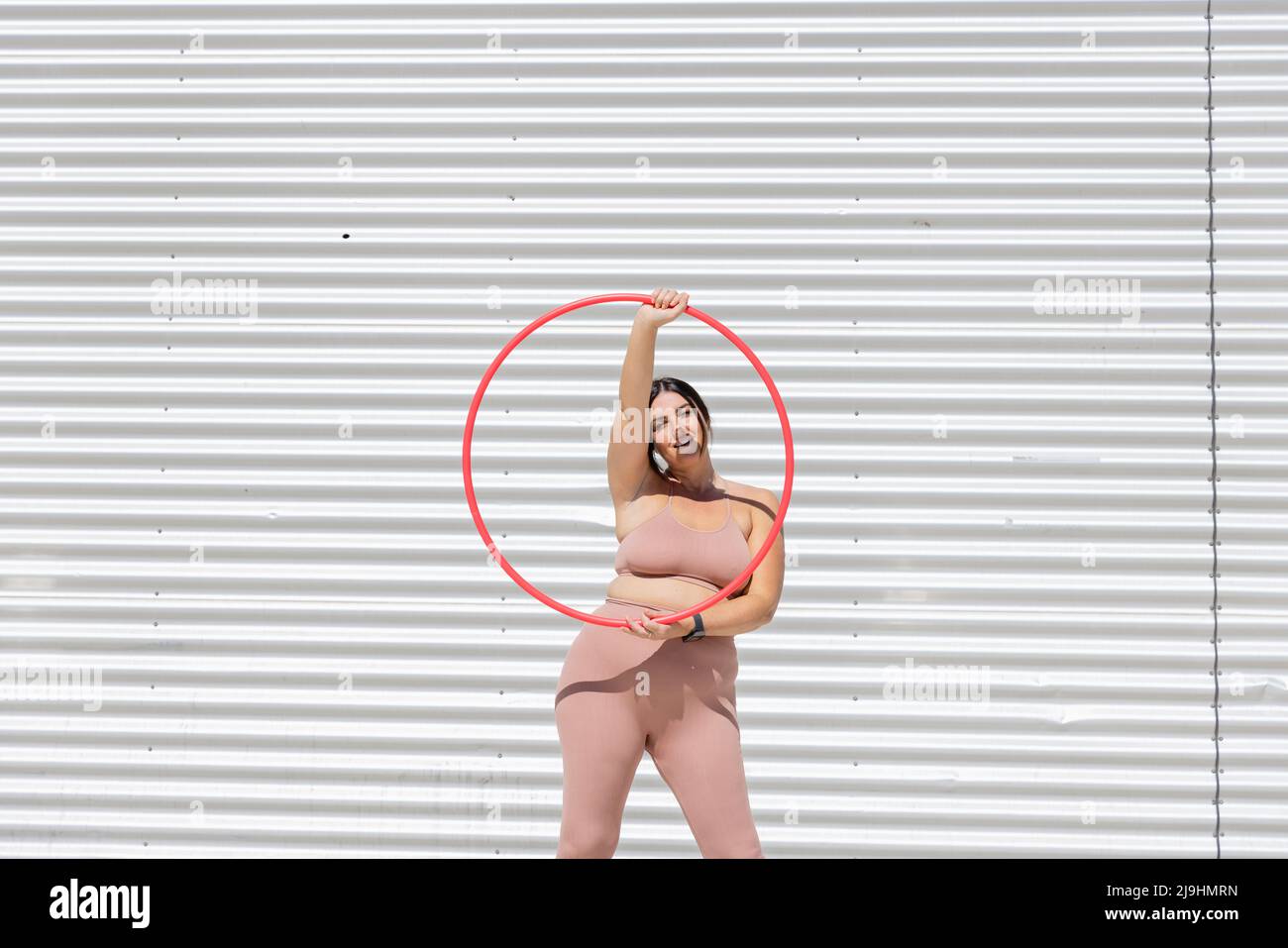 Kurvige Frau mit Kunststoffreifen vor der Wellwand Stockfoto
