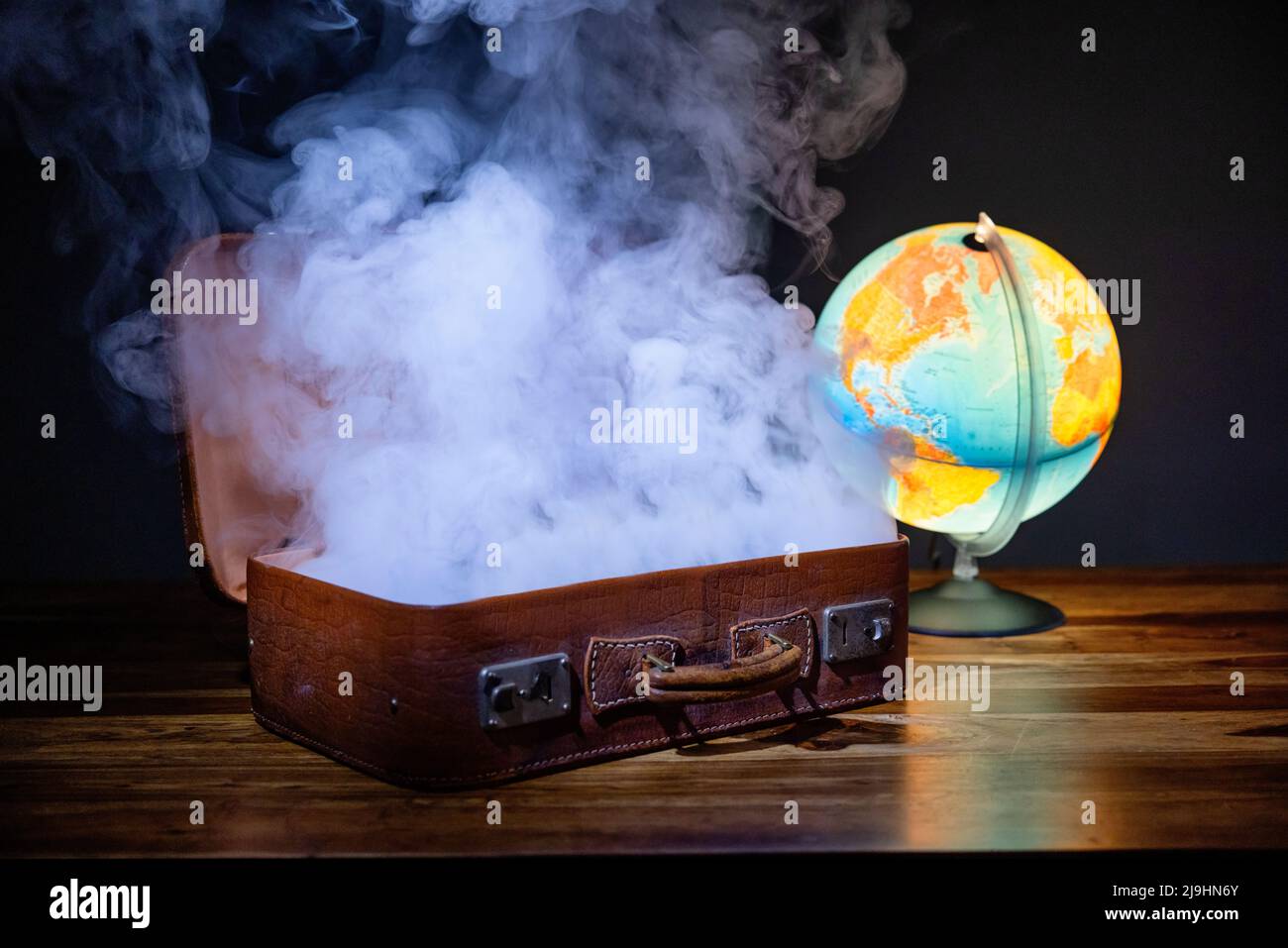Studioaufnahme von glühendem Globus und Rauch, der aus dem offenen Koffer steigt Stockfoto