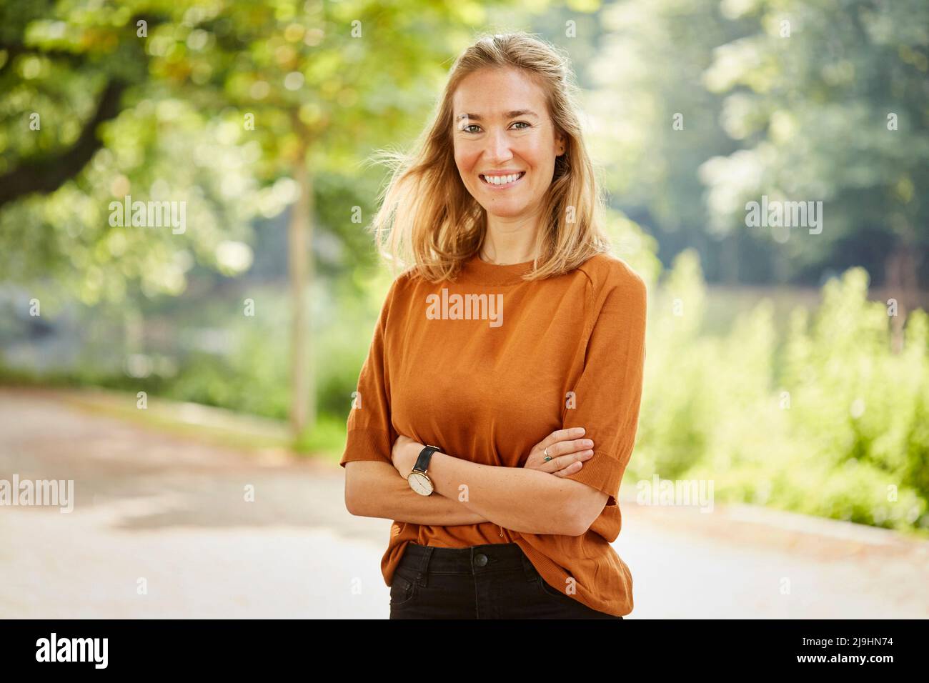 Glückliche Frau mit gekreuzten Armen im Park stehend Stockfoto