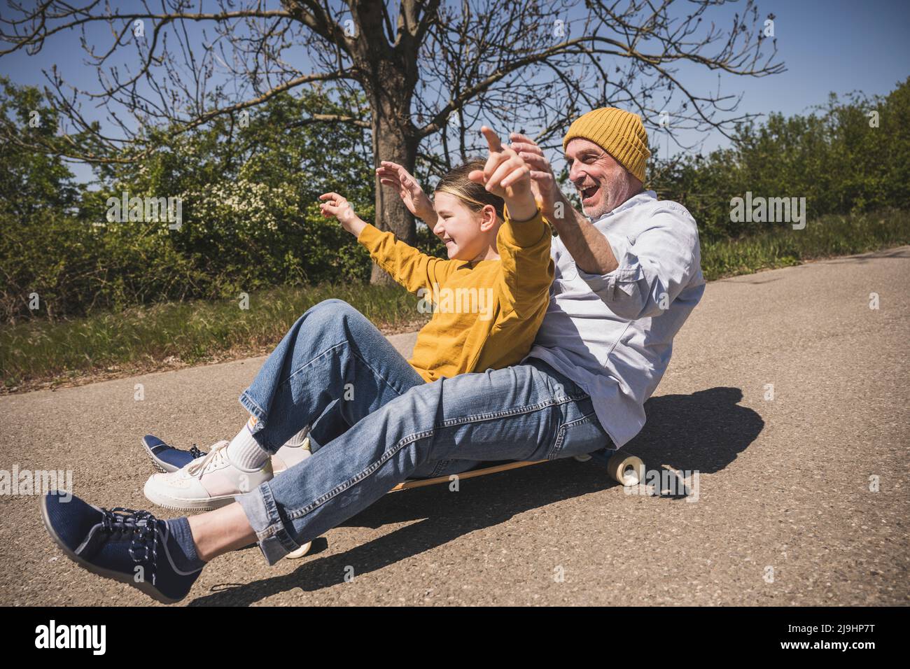 Fröhlicher älterer Mann genießt Skateboarding mit Enkelin auf der Straße Stockfoto