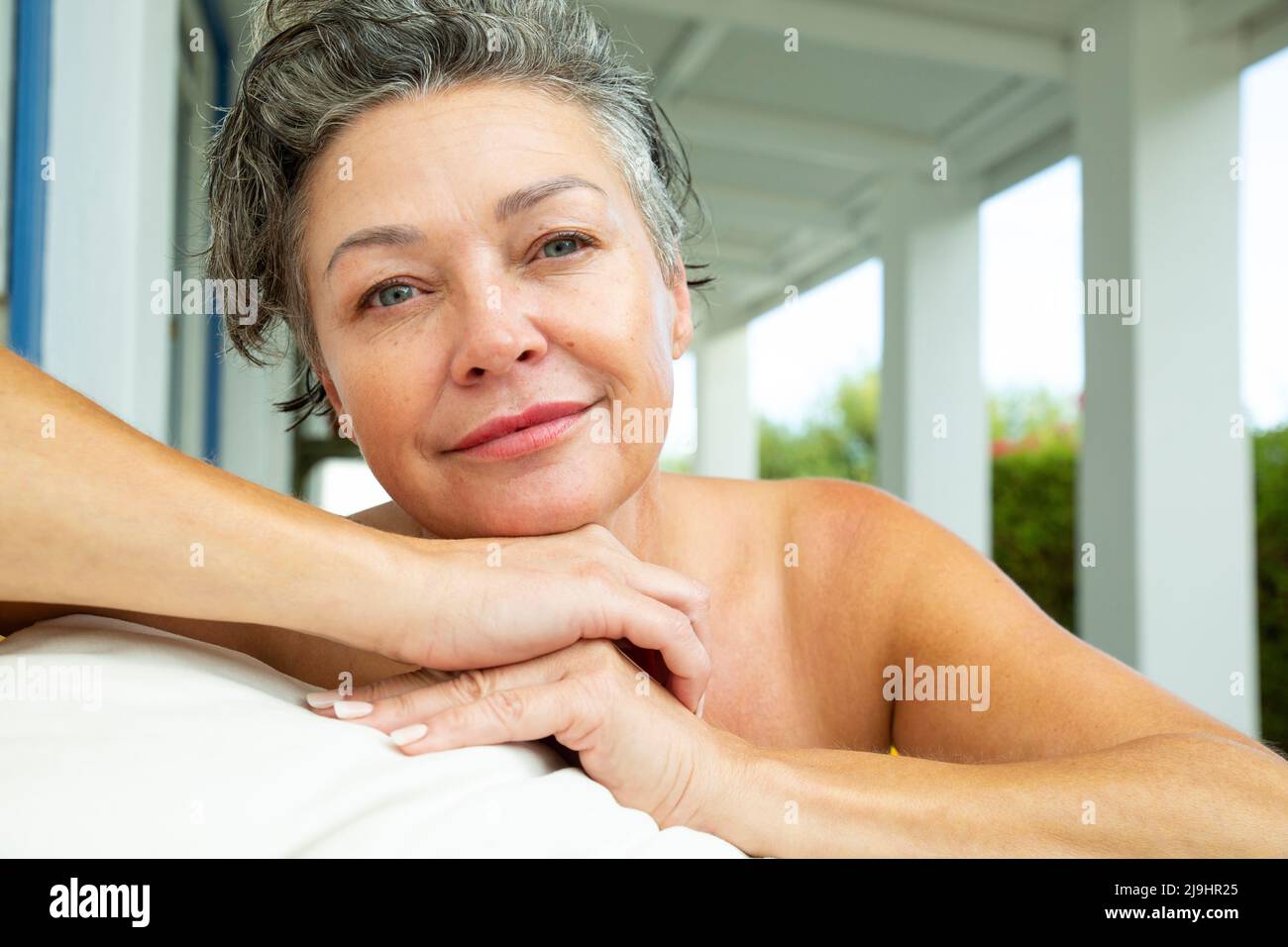 Lächelnde, reife Frau mit Kissen, die zu Hause auf der Veranda sitzt Stockfoto
