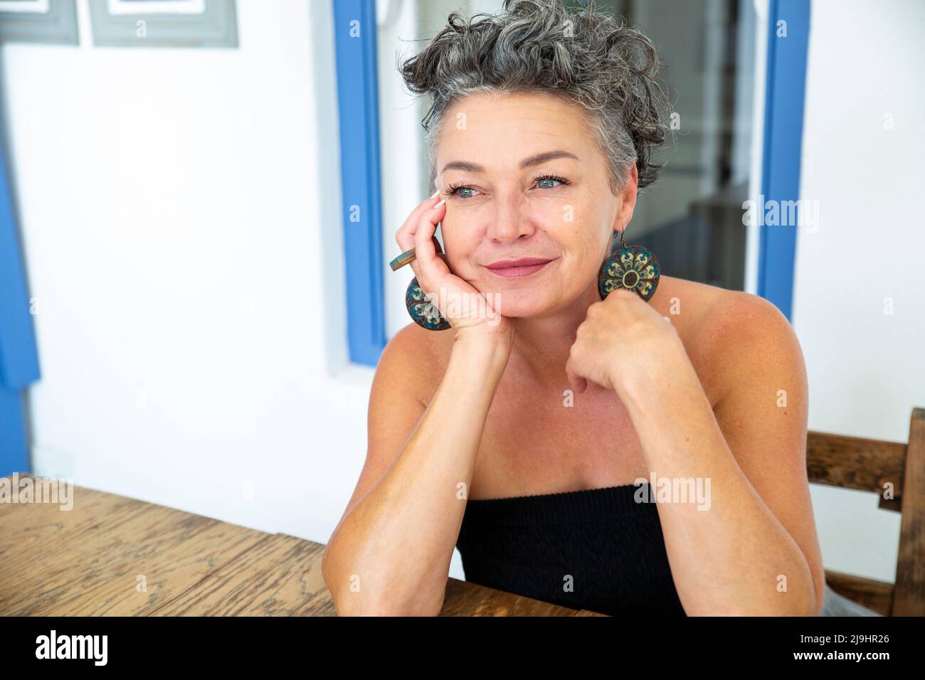 Lächelnde Frau mit kurzen Haaren sitzt am Tisch Stockfoto