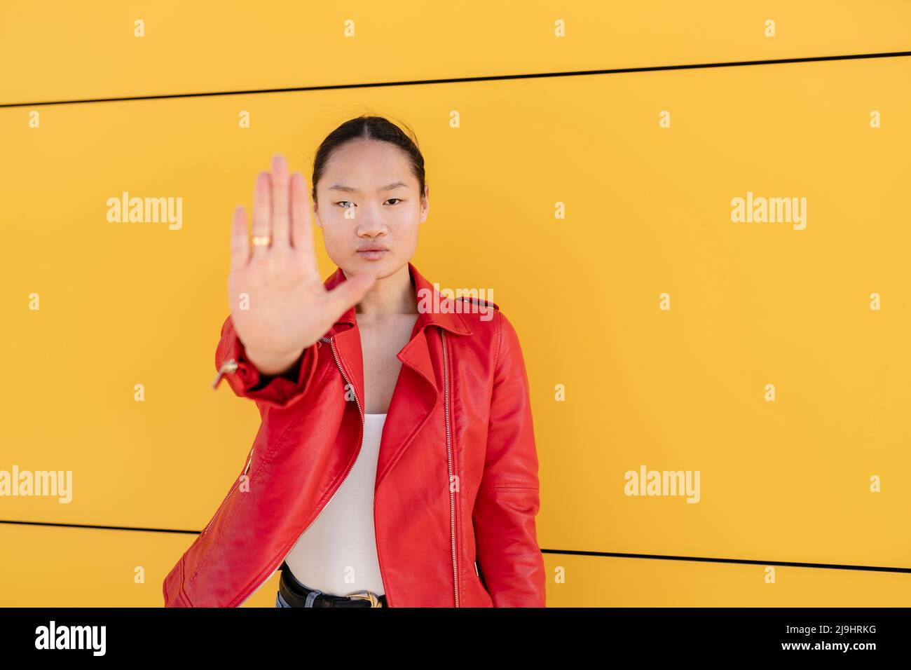 Junge Frau, die mit der Hand vor der gelben Wand ein Stoppschild gestikuliert Stockfoto