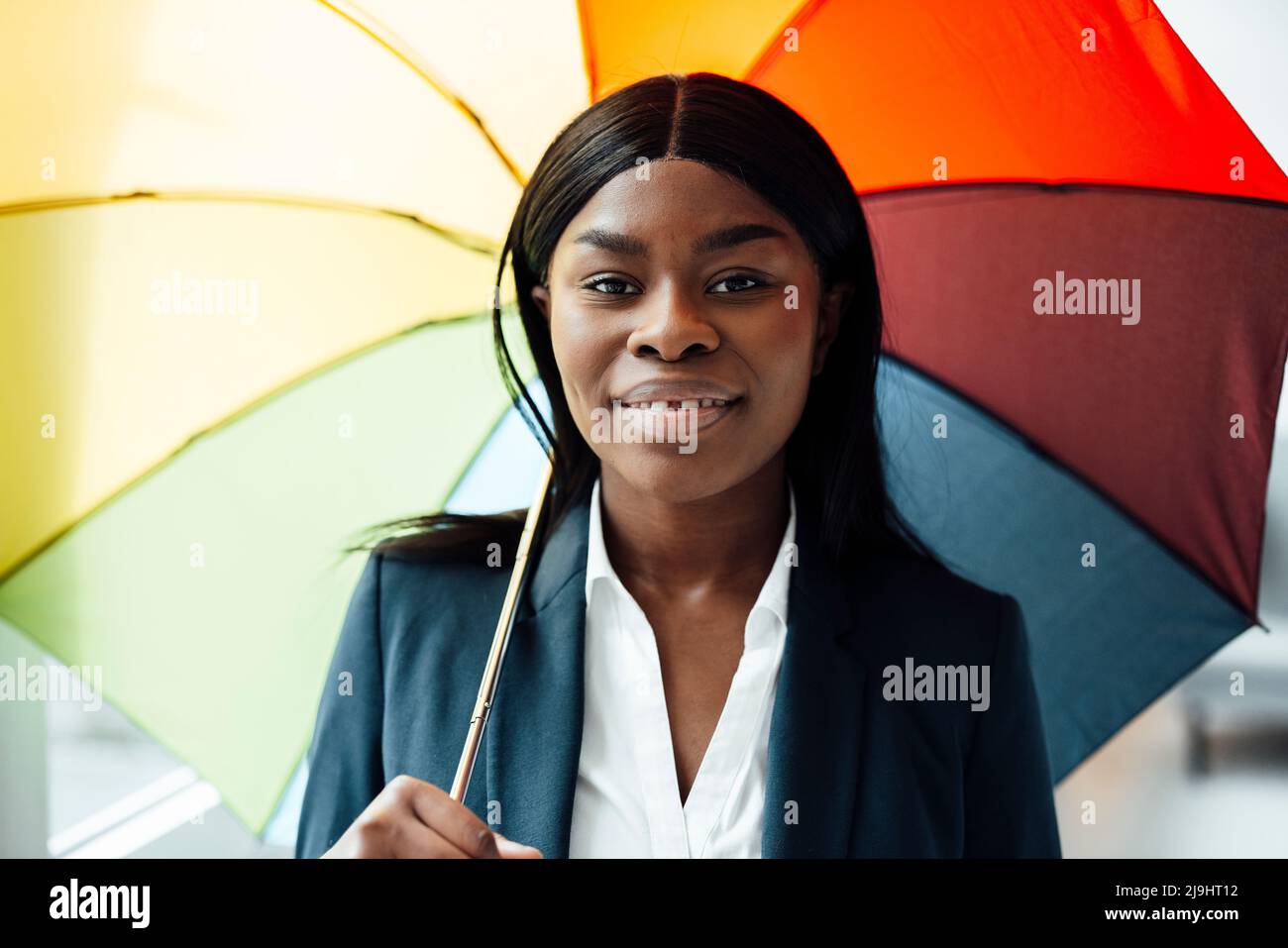 Lächelnde Geschäftsfrau mit buntem Regenschirm im Büro Stockfoto