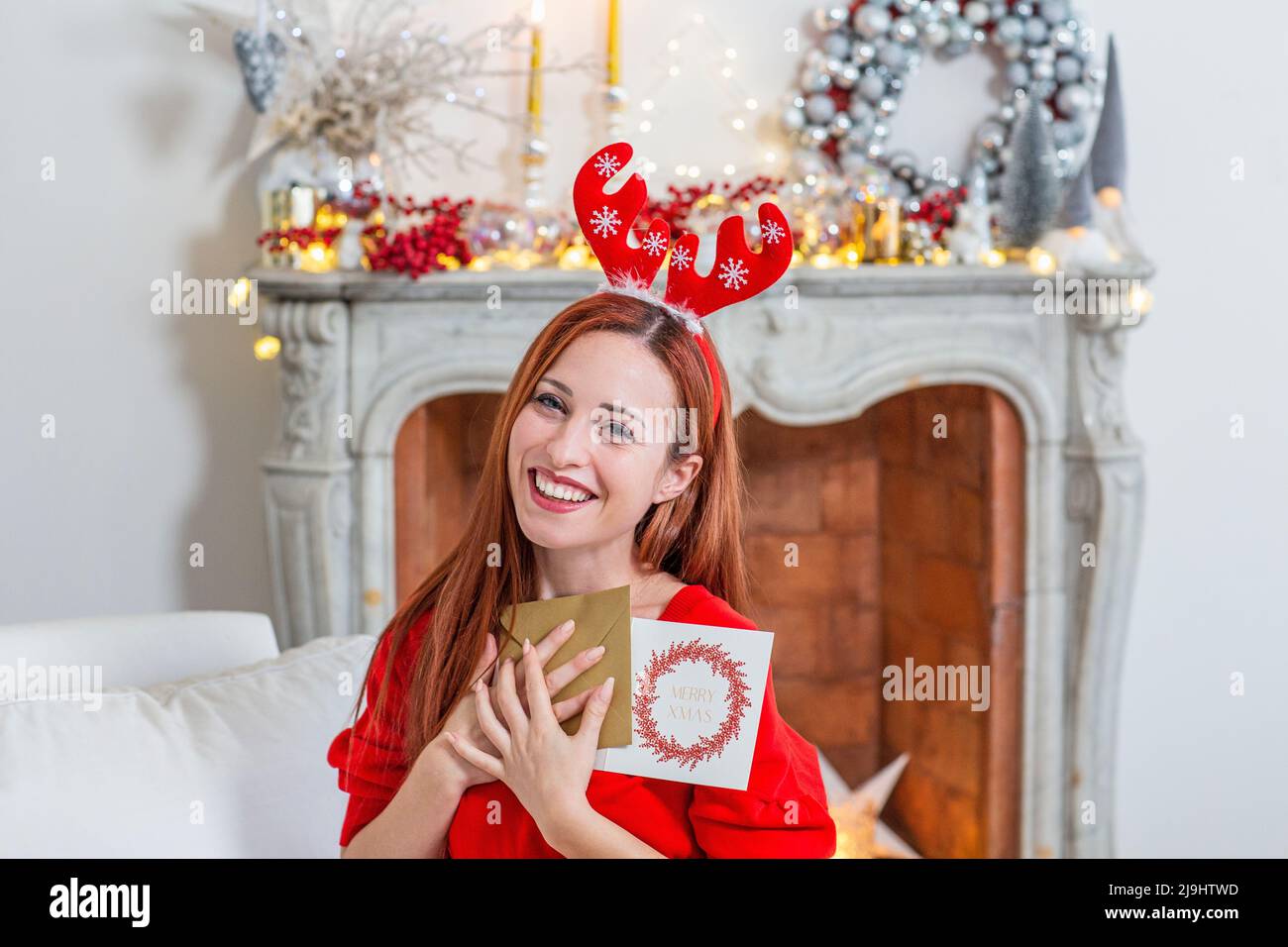 Glückliche Frau trägt Weihnachtsschmuck mit Grußkarten zu Hause Stockfoto
