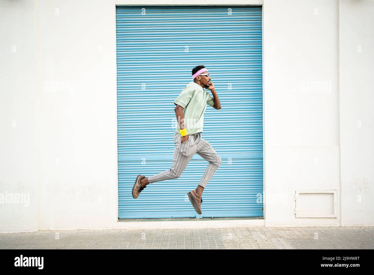 Junger Mann mit der Hand in der Tasche springt mitten in der Luft auf dem Fußweg Stockfoto