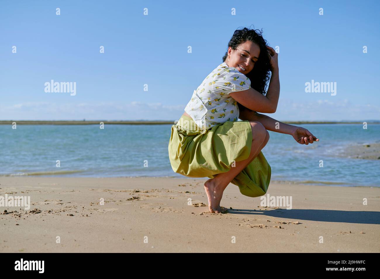 Lächelnde junge Frau, die am Strand auf Zehenspitzen hocken kann Stockfoto