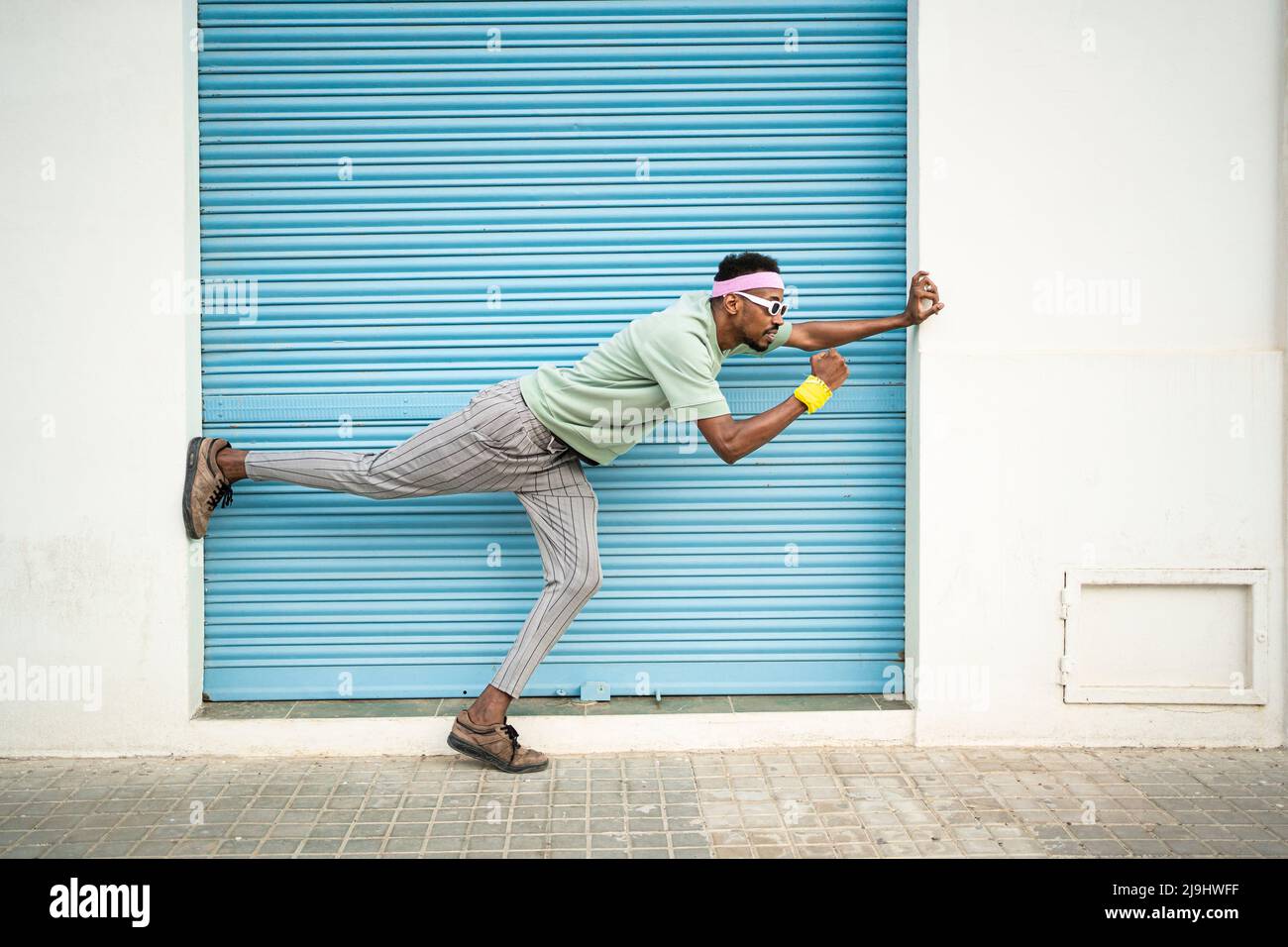 Verspielter junger Mann, der auf einem Bein vor dem blauen Verschluss steht Stockfoto