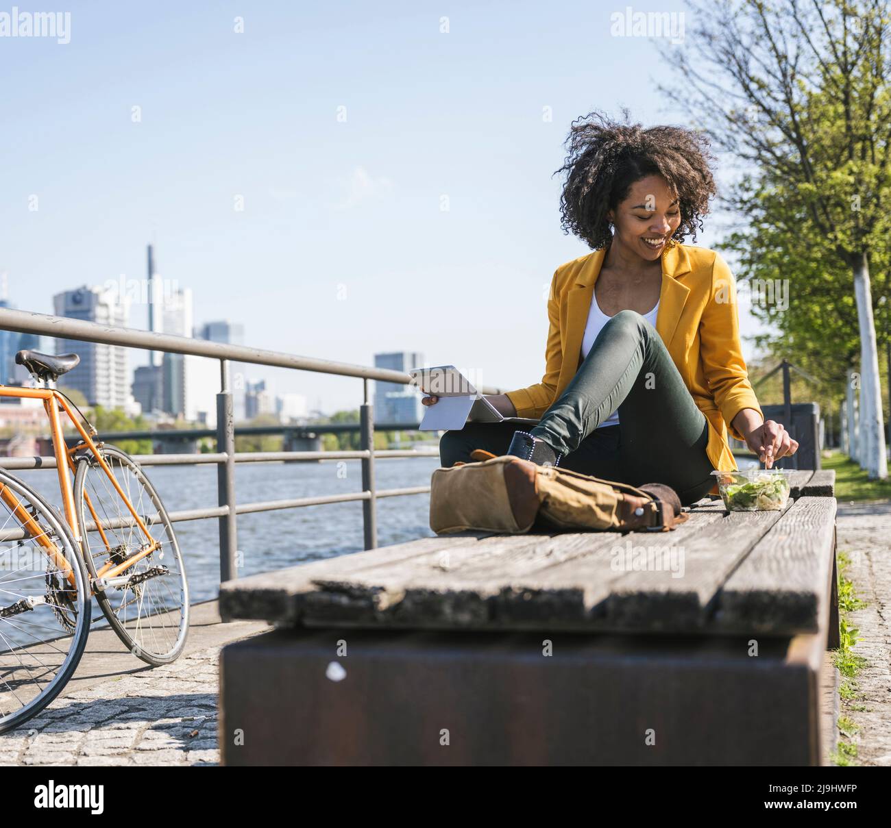 Junge Geschäftsfrau mit Laptop, die Essen auf der Bank hat Stockfoto