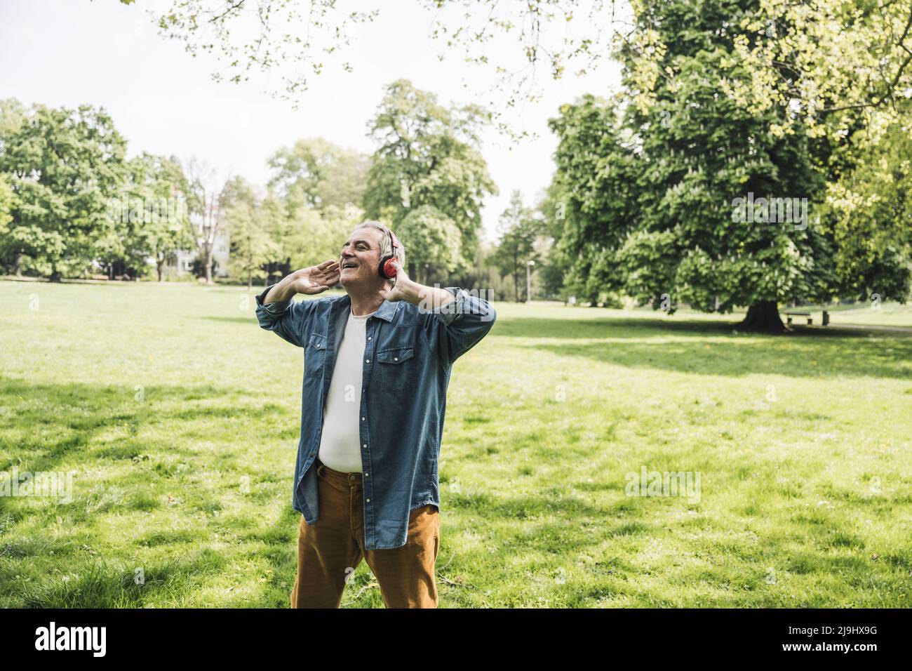 Glücklicher Rentner mit kabellosen Kopfhörern, der im Park Musik genießt Stockfoto
