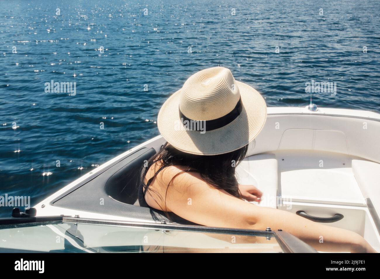 Frau in Strohsonnenhut sitzt im Bug des Freizeitbootes und blickt auf das Wasser Stockfoto