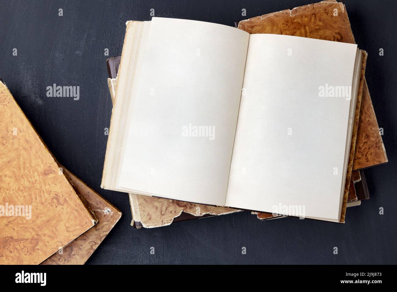 Vintage Notizbuch mit leeren Seiten liegt auf einem Stapel schäbiger Bücher auf einem schwarzen Betontisch Stockfoto