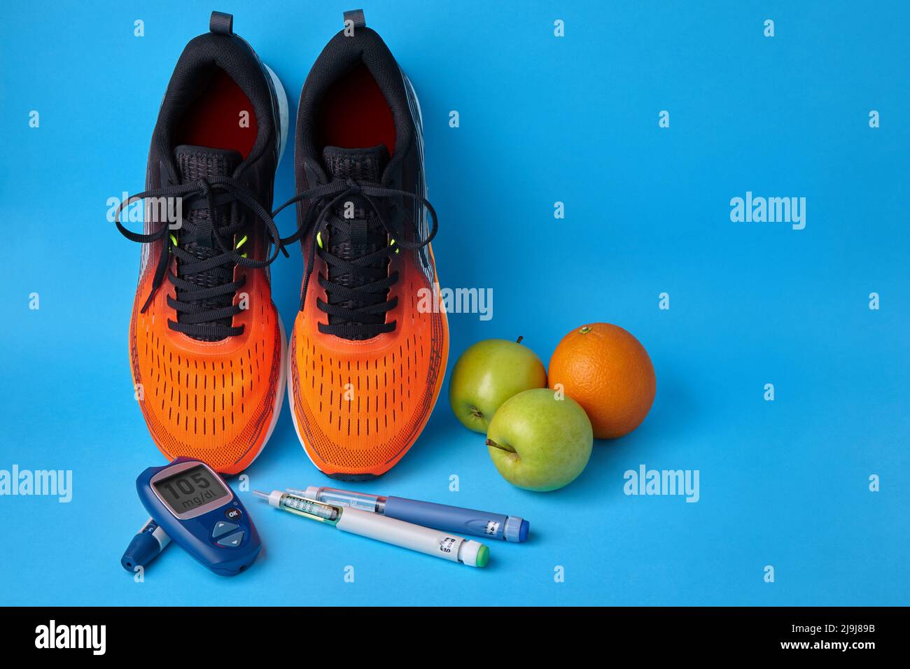 Orangefarbene Sneakers, Früchte, Glucometer und Insulin-Spritzenstifte auf blauem Hintergrund Stockfoto