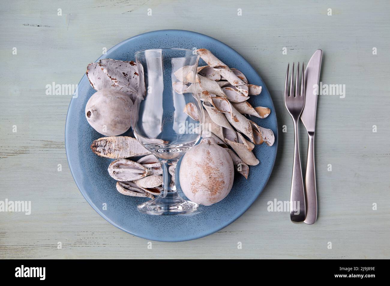 Blauer Teller mit getrockneten und farbigen exotischen Früchten, leerem Glaskelch und Besteck auf einem Holztisch Stockfoto