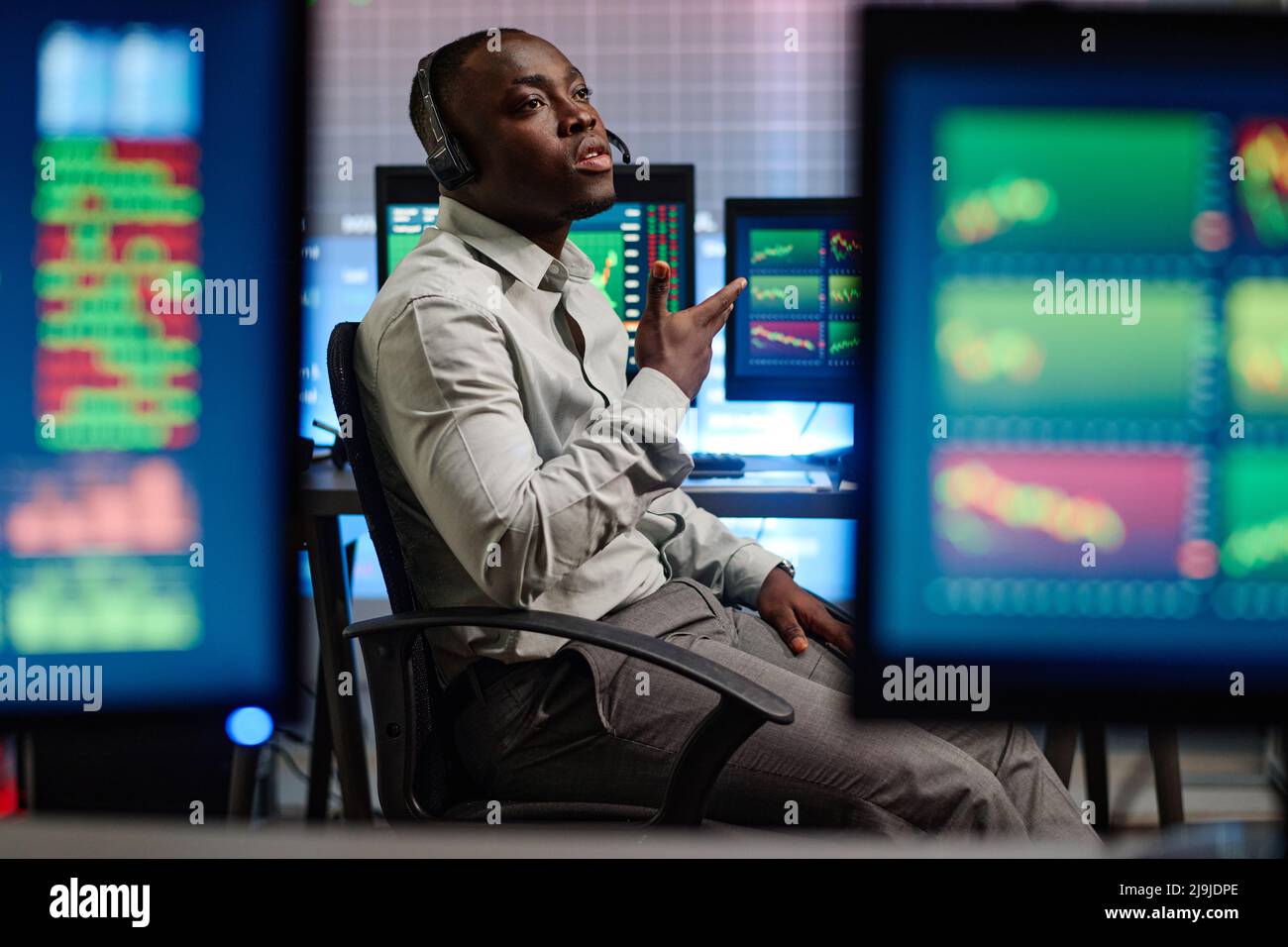 Junger afroamerikanischer Mann, der in einem modernen Maklerunternehmen arbeitet, hat Probleme mit seinem Kunden, der versucht, das Problem telefonisch zu erklären Stockfoto