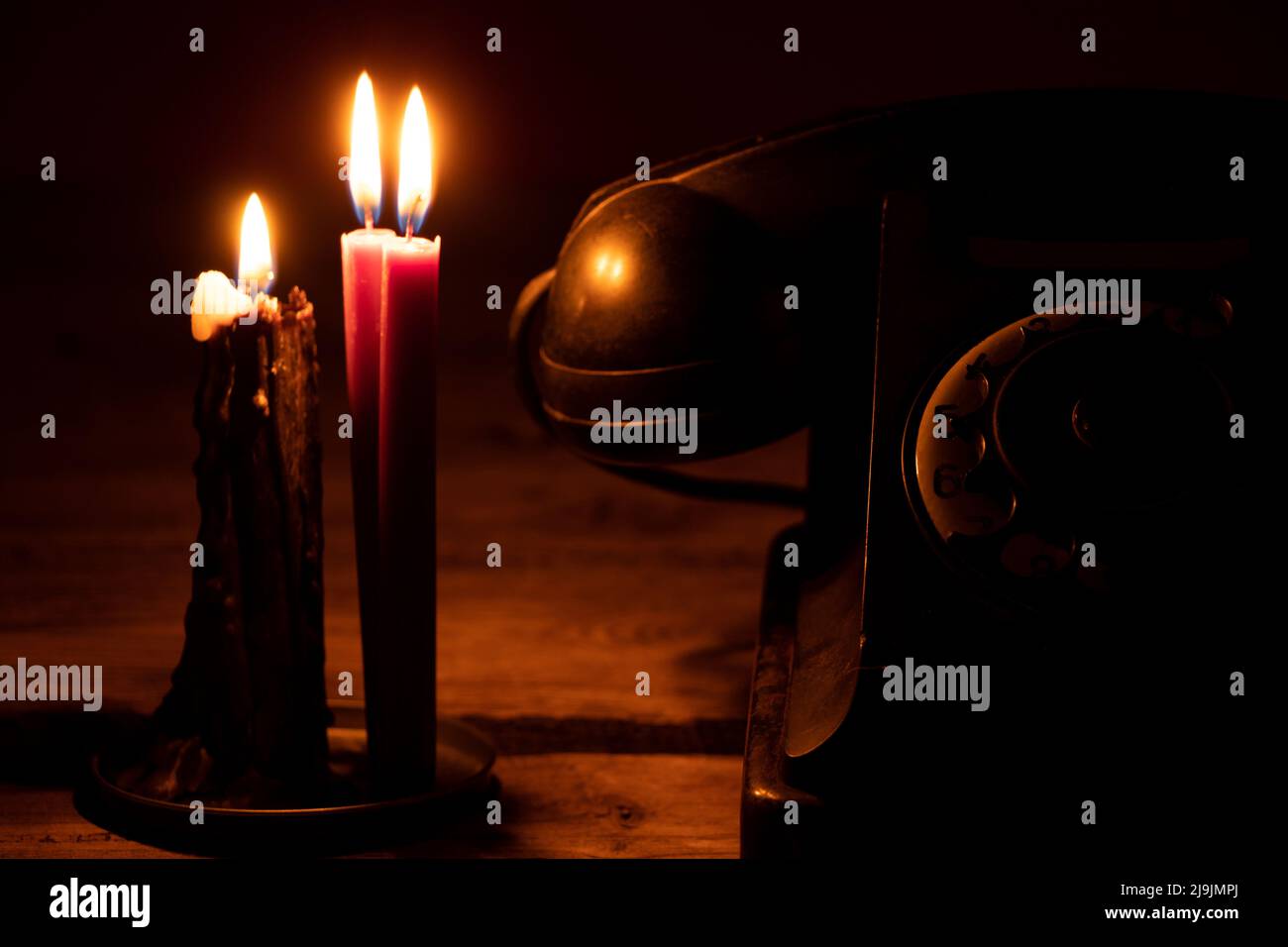 Altes schwarzes Retro-Telefon auf einem Holztisch im Dunkeln in der Nähe der Kerzenflamme, Telefon und Technologie, Telefon klingelt im Dunkeln Stockfoto