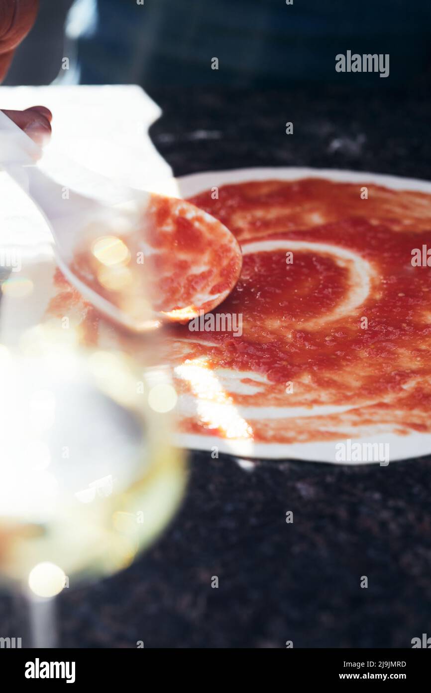 Der Pizzateig ist mit Tomatensauce überzogen. Der Prozess der Herstellung von hausgemachter Pizza. Das Konzept der hausgemachten Fast Food. Vertikales Foto. Stockfoto