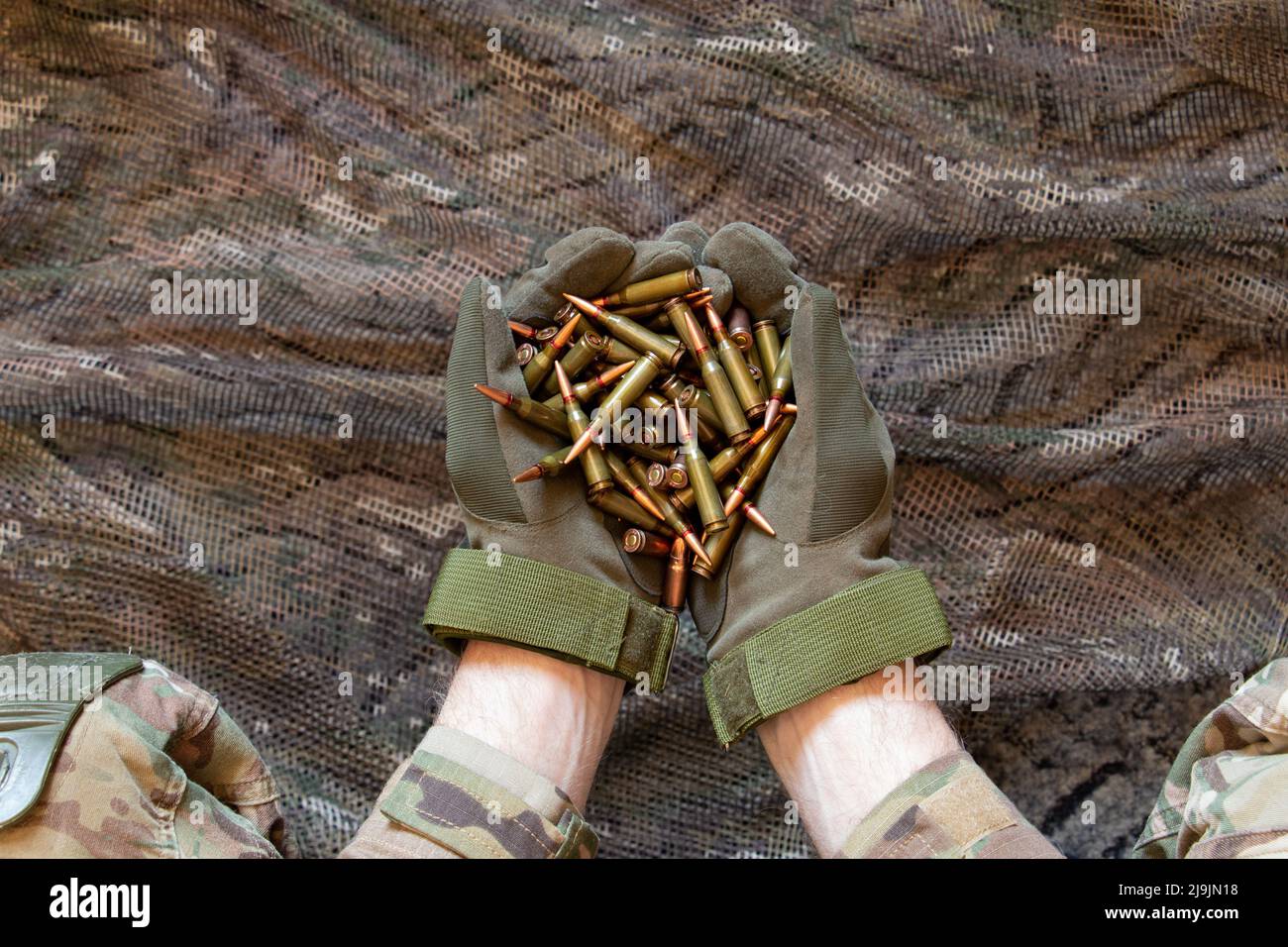 Ukrainischer Soldat in Handschuhen hält Kugeln aus einem Maschinengewehr auf einem Tarnhintergrund, Waffen der ukrainischen Armee, Krieg in der Ukraine 2022 Stockfoto
