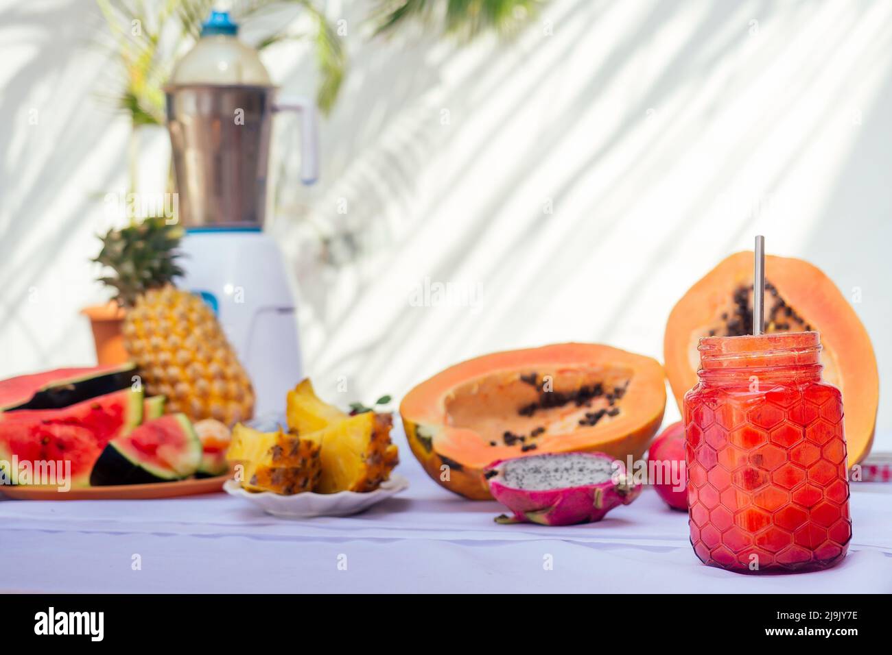 Tropische Früchte Zutaten Granatapfel, Ananas, Papaya, Drachenfrucht, Orange und Wassermelone mit Mixer auf weißem Tisch Sommerhintergrund Palmblatt Stockfoto