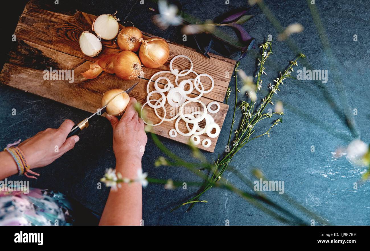 Eine Menge Zwiebeln in einem Korb und Teller auf einem dunklen und eleganten dunklen Strukturhintergrund. Zwiebeln und Scheiben auf Holzschneidebrett anbraten. Stockfoto