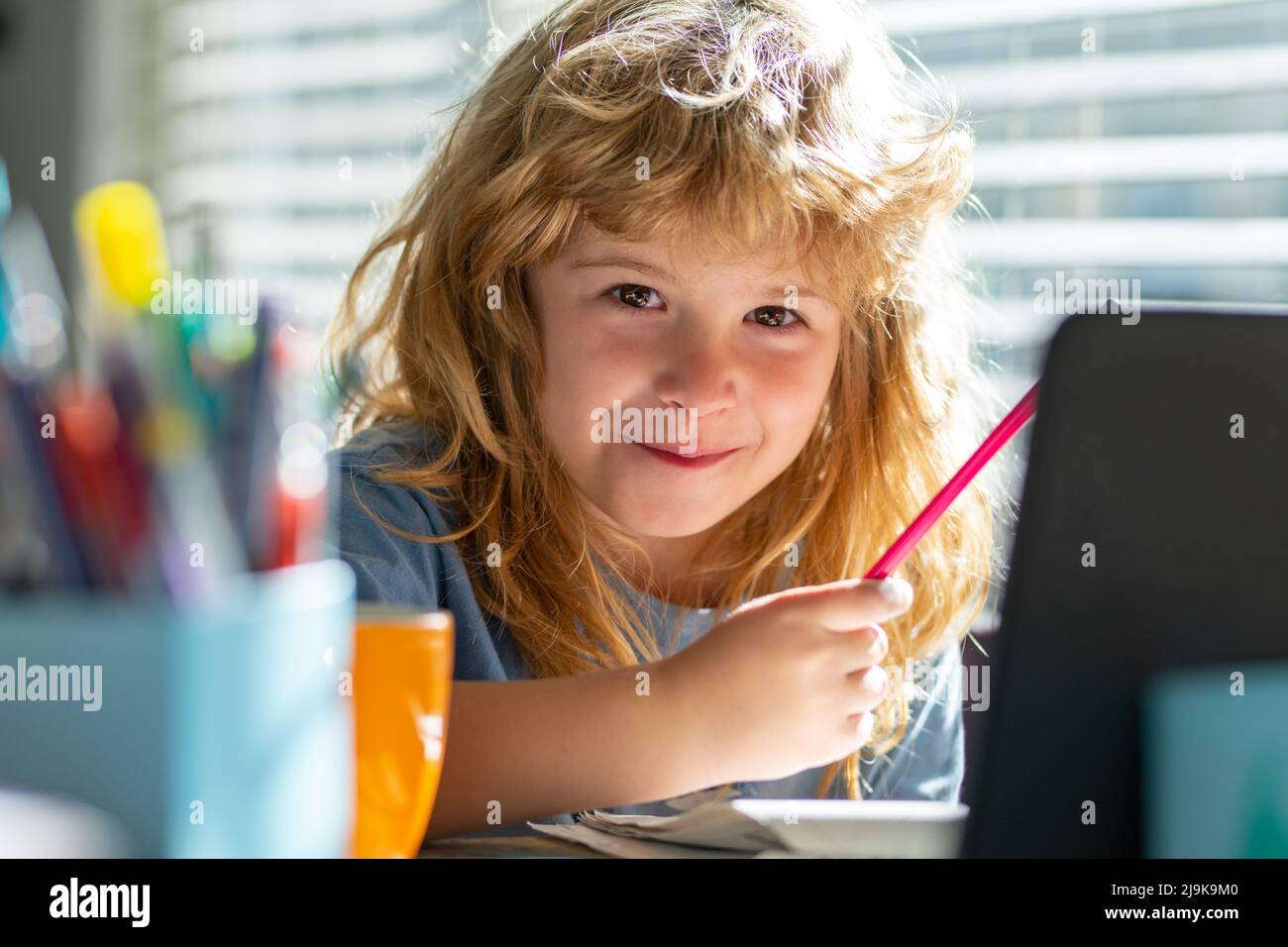 Porträt eines Schuljungen, der auf dem Tisch sitzt und Hausaufgaben macht. Kind mit Bleistift und Schrift. Junge, der auf weißem Papier am Tisch zeichnet. Elementar Stockfoto