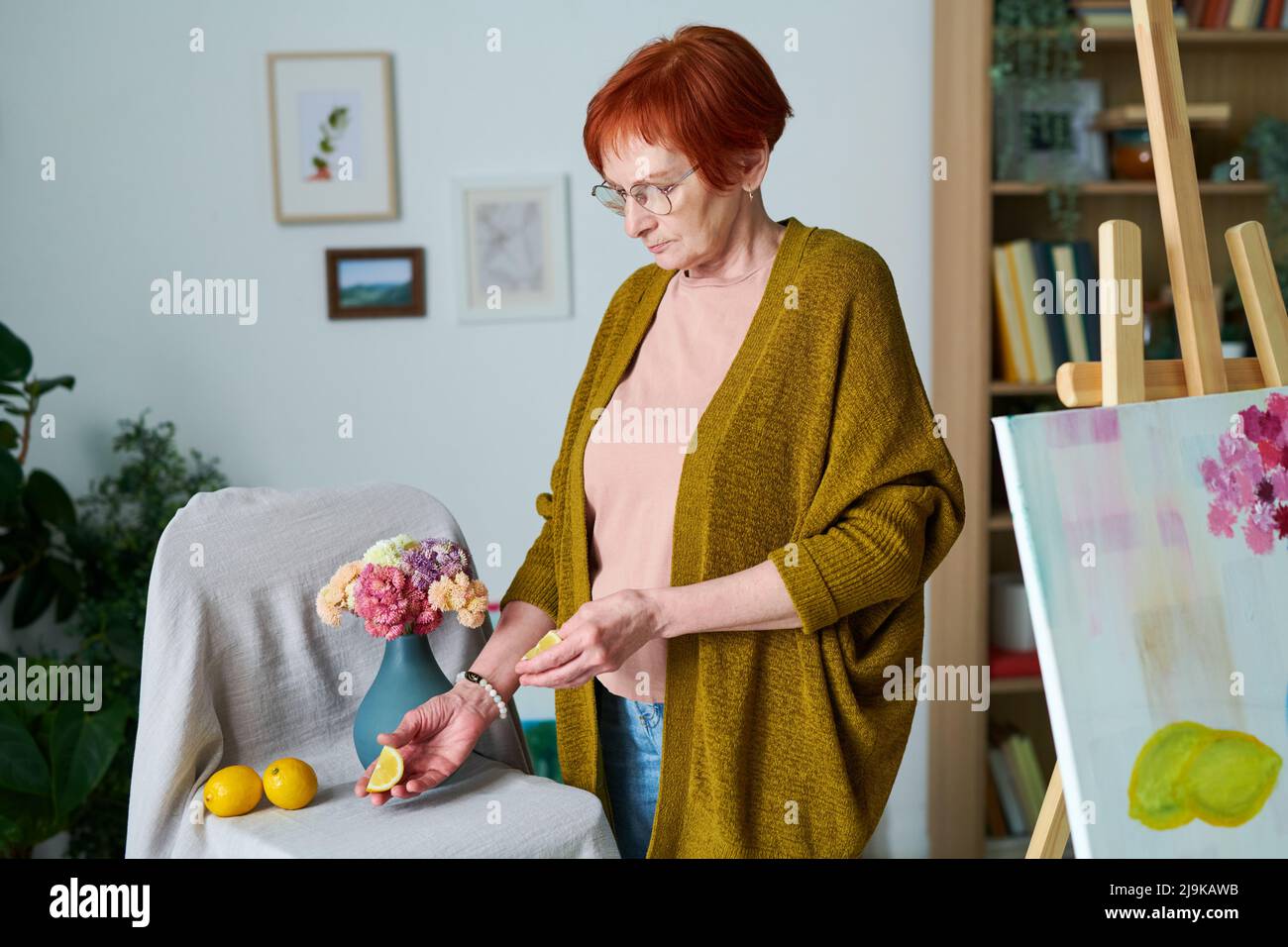 Ältere Frau in Brillen, die aus Zitronen und Blumen in der Vase Stillleben macht, bevor sie zu Hause malt Stockfoto