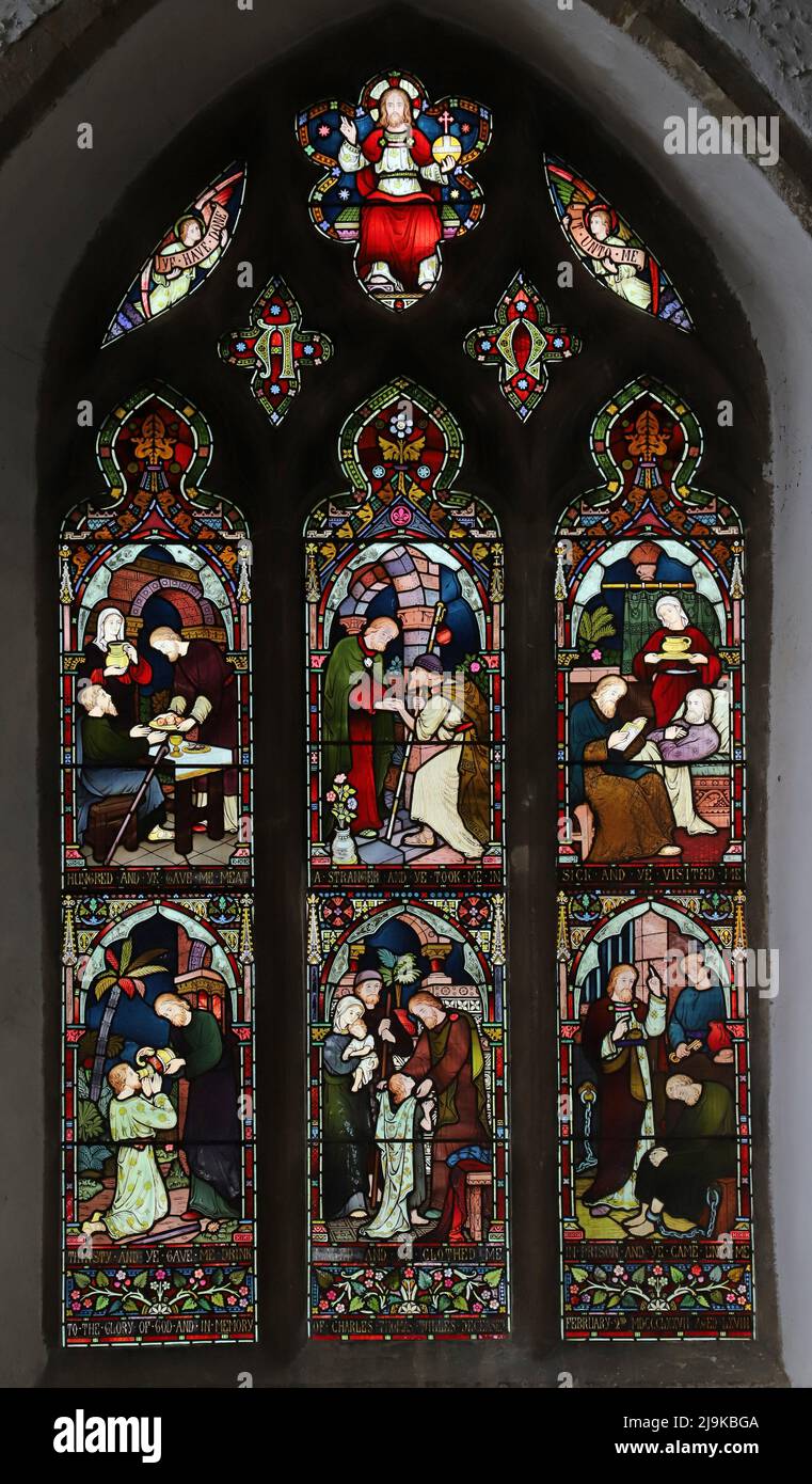 Ein Buntglasfenster von Frederick Preedy, das 6 Acts of Corporal Mercy, Saints Peter and Paul Church, King's Sutton, Northamptonshire, darstellt Stockfoto